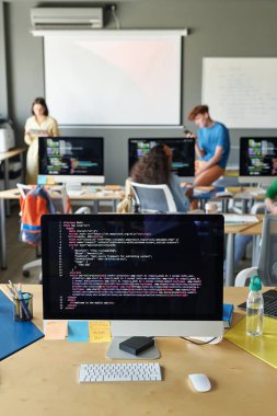 Sınıfta arka planda öğrenciler ve öğretmenle birlikte monitörlü bilgisayarın dikey görüntüsü