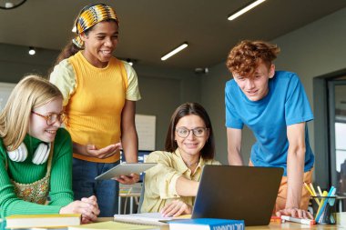 Sınıftaki IT dersinde öğretmenle yazılım tartışan bir grup öğrenci.