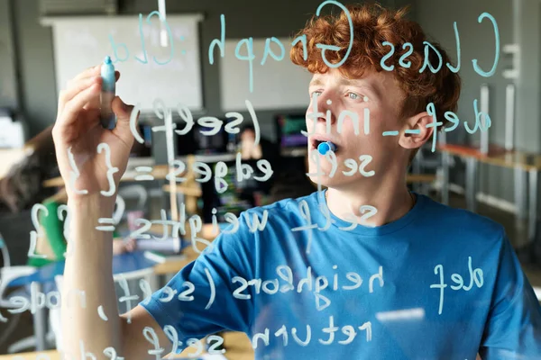 教室でのItレッスン中にガラス壁にコンピュータコードを書く学生 — ストック写真