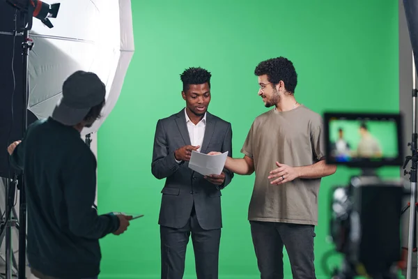 Afrikalı Amerikalı sunucu profesyonel stüdyoda dururken yönetmenle senaryoyu tartışıyor.