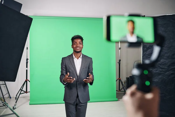 African American man in suit recording video content on smartphone in professional studio