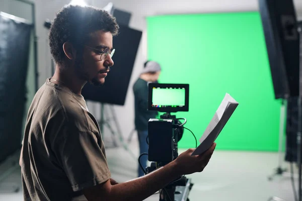 Young professional cameraman reading script before shooting in studio