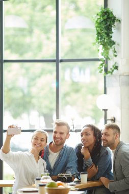 Modern, rahat bir kafede grup selfie 'si yapan iyimser, genç, çok ırklı arkadaşlar.