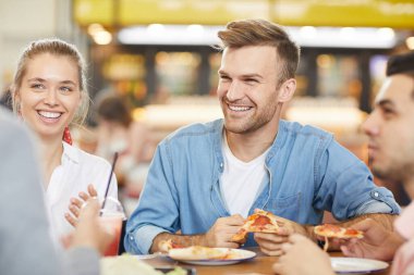 Bir grup neşeli heyecanlı arkadaş fast food restoranında masada oturup sohbet ederken pizza yiyorlar.