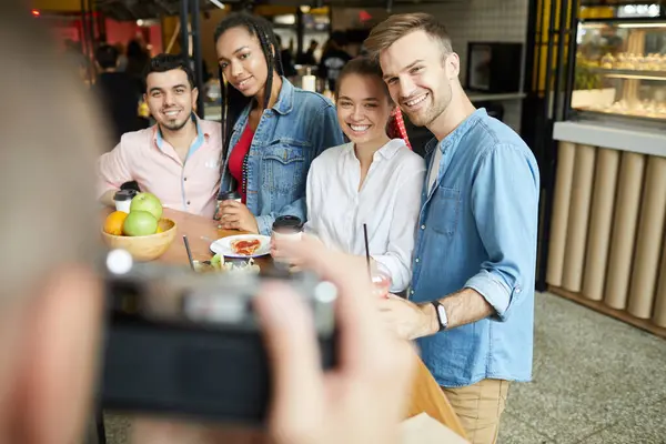 Group of young interracial friends standing at counter in modern cafe and posing for photo