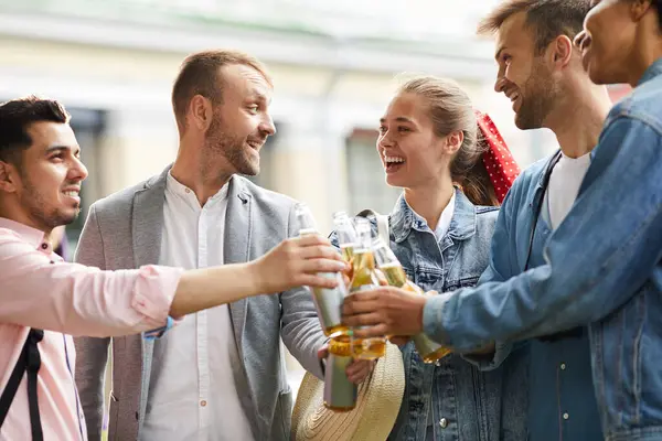 Group of excited young friends in casual clothing standing together and having fun with beer