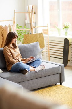 Kahverengi saçlı, yetenekli genç bir kadın. Dizüstü bilgisayar kullanıyor. Kendi marka kıyafetleri üzerinde çalışıyor.