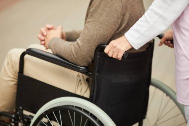 Dışarıda dolaşırken tekerlekli sandalyeyi engelli hastalarla iten tanınmayan tıbbi hemşirelerin yakın çekimi.