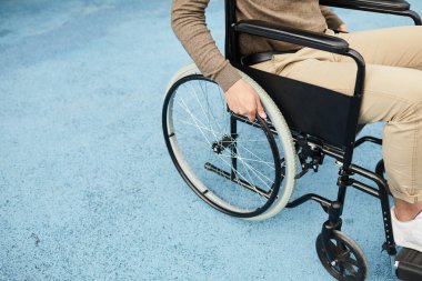 Tanımlanamayan, sıradan kıyafetli, tekerlekli sandalyeyle gezen felçli bir adamın yakın çekimi.