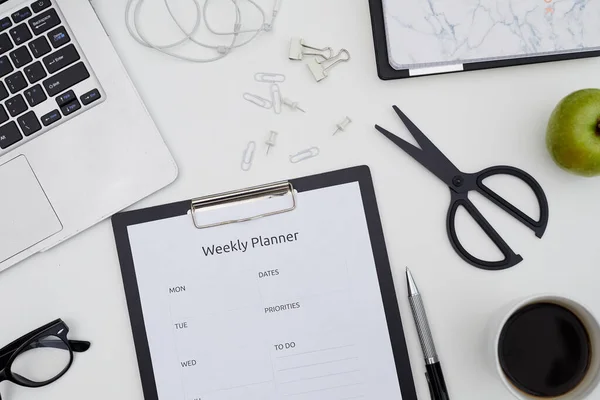 Directly above view of clipboard with weekly planner paper, scissors, paper pins, coffee cup on table