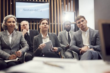 Formalite icabı çok ırklı iş adamlarından oluşan ciddi bir grup konferans odasında oturup dikkatle konuşmacıları dinliyor.