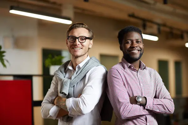 Positive confident young multi-ethnic startuppers standing back to back and looking at camera in office