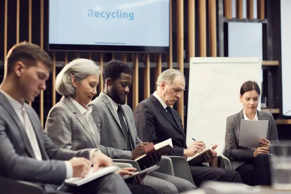 Group of content multi-ethnic business people in formal outfits sitting in line and making notes while performing creative task at training class