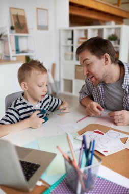 Tatmin olmuş genç bir baba ve tatlı bir oğul oturma odasında oturuyor ve anne için el yapımı sevgililer günü kartı hazırlıyorlar.
