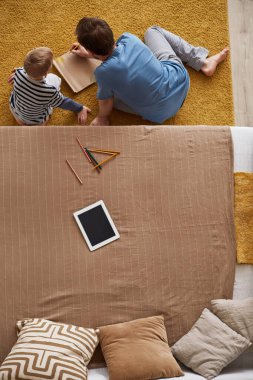 Babamın, oğluyla birlikte pijamalarıyla halının üzerinde oturduğu ve çizim defterine çizim yaptığı resmin tam üstünde.