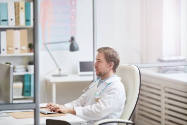 Ofiste çalışırken masasında sakalları olan ve klavyeyle yazı yazan çok meşgul genç bir cerrah.