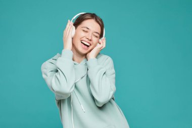 Kapüşonlu neşeli genç kadın kulaklıkla müzik dinlerken gözlerini kapatıyor ve gülüyor.