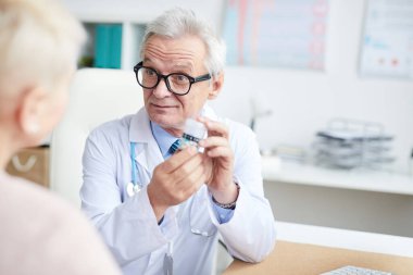 Konsültasyonda hastaya ilaç yazarken kaşlarını çatan gözlüklü kıdemli hekim.