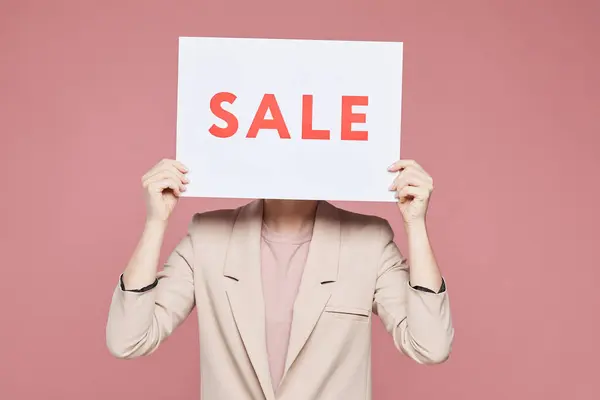 穿着时髦夹克的女人站在粉色背景下 躲在销售横幅后面 — 图库照片