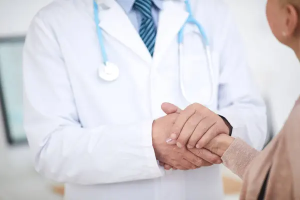 Laboratuvar önlüklü, tanınmayan erkek doktorun yakın plan fotoğrafı. Ayakta ve hastanın elini tutarken onu destekliyor.