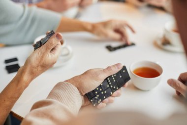 Masada oturan ve elinde domino taşları tutan yaşlı bir kadın, huzurevindeki domino turnuvasına katılıyor.