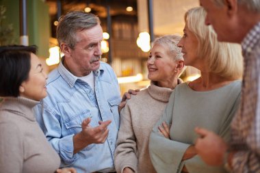 Kot gömlekli, kendine güvenen yaşlı bir adam, arkadaşlarıyla ilginç bir hikaye paylaşırken bayan arkadaşının omzuna dokunuyor.