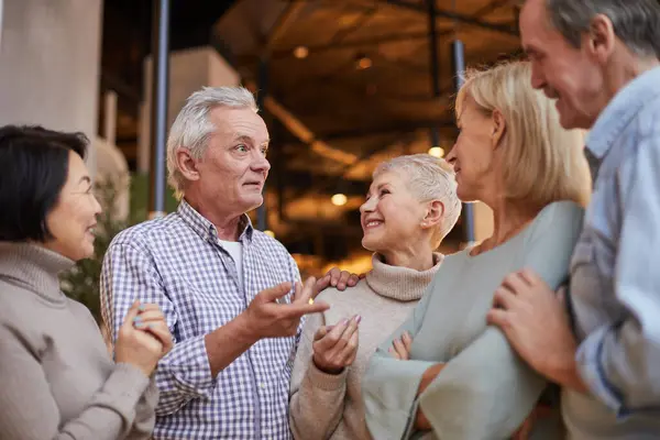 Group of emotional elderly friends in casual clothing standing in circle and discussing news