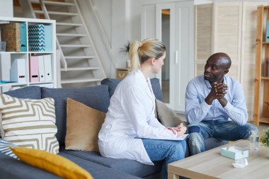 Yakışıklı, genç, Afro-Amerikalı bir adam kanepeye oturmuş terapi seansında kadın psikologla konuşuyor.