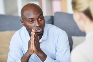 Tişörtlü, dalgın, kel iş adamının yakın planda el ele tutuşması ve terapi seansında psikologla konuşması.