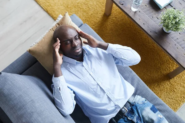 Above view of troubled young Afro-American man in shirt lying on psychiatrists couch and massaging temples at therapy session