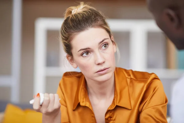 Sorrowful young woman in orange blouse holding napkin and asking question to psychologist at therapy session