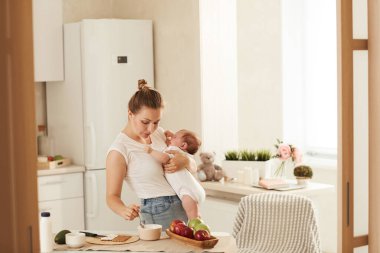 Beyaz tişörtlü, bebeğini kucağında tutarken hızlı yemeye çalışan meşgul bir annenin kahvaltısı.