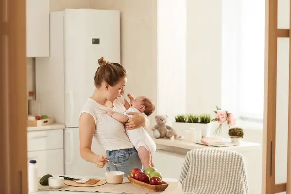 Young mother in white Tshirt truing to cheer up her baby who is crying and doesnt want to eat