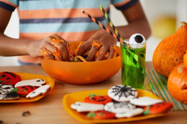 Tanımlanamayan siyah bir çocuğun plastik örümcek yüzükleriyle parmaklarını şeker kasesine koyduğu yakın plan.