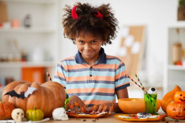 Kırmızı boynuzlu, sinsi zenci bir çocuğun portresi. Elinde balkabakları ve şekerlerle Cadılar Bayramı için hazırlanıyor.