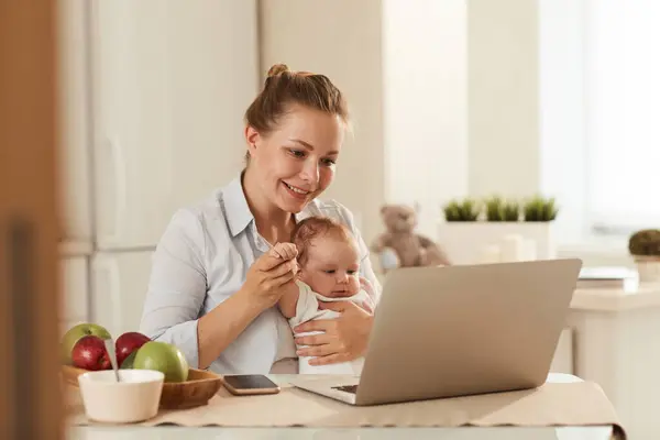 Young smiling mother in showing cartoons on laptop to little baby