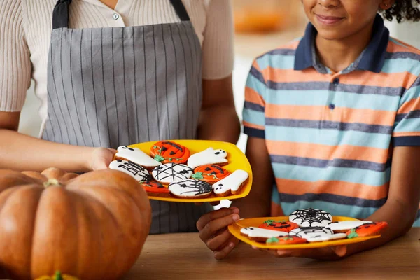 Close-up of Afro-American family standing at table and holding plates with creative gingerbread cookies for Halloween