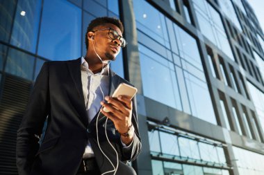 Kulaklıkla sesli mesaj dinleyen düşünceli genç siyahi iş adamının görüş açısının altında.