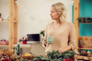 Dalgalı sarı saçlı, Noel süslemeleriyle masasında duran ve Noel atölyesinde kahve içerken gözlerini kaçıran dalgın, genç ve güzel bir kadın.