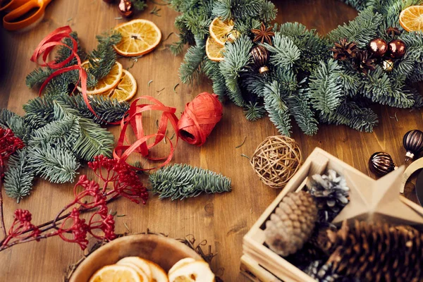 Workplace for Christmas wreath making: close-up of decorative paper ribbon, berry twig, coniferous branches and balls on table