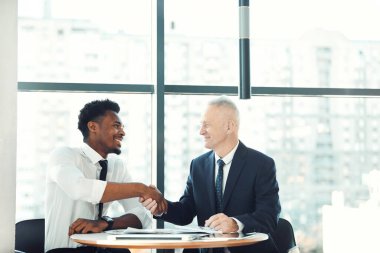 Çok uluslu iş adamları resmi giysiler içinde masada oturup önemli bir sözleşme imzaladıktan sonra tokalaşıyorlar.