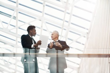 Genç Afro-Amerikalı uzman. Kontrat konularında koridorda duruyor ve üst düzey yöneticilerle görüşüyor.