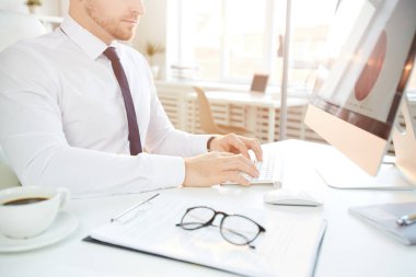 Resmi tişörtlü genç iş adamının ofis masasında oturup bilgisayarda çizelgeler oluştururken görüntüsü.