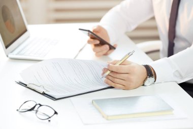 Kol saatindeki tanınmayan yöneticinin ofis masasında oturması ve ofis belgeleriyle çalışırken zaman çizelgesini çevrimiçi takvimde kontrol etmesi