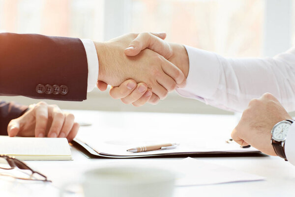 Крупный план неузнаваемого бизнес-руководителя, сидящего за столом и пожимающего руку деловому партнеру после заключения успешной сделки