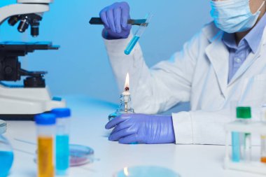 Laboratuvarda laboratuvar önlüklü tanınmayan kimyagerin yakın plan fotoğrafı ve gaz ocağının üzerinde ısıtma maddesi var.