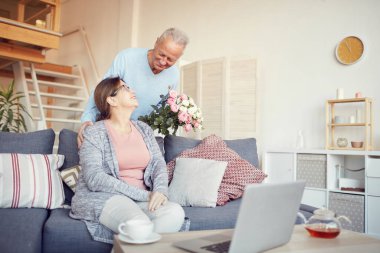 Gülümseyen yakışıklı adam evde yıldönümünü kutlarken karısına güzel bir buket çiçek veriyor.