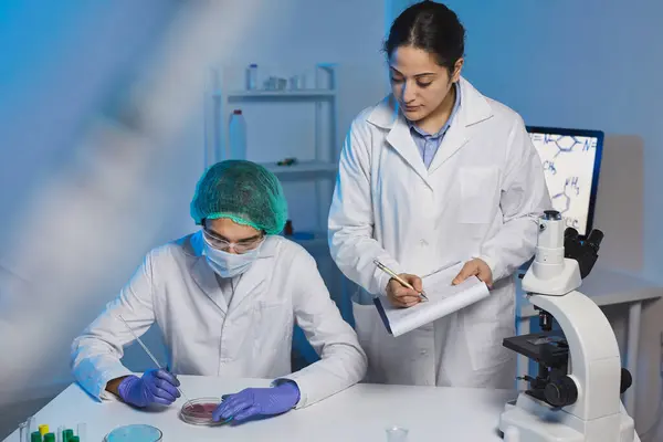 Team of young multi-ethnic clinical researchers in lab coats working with medical substances in modern laboratory