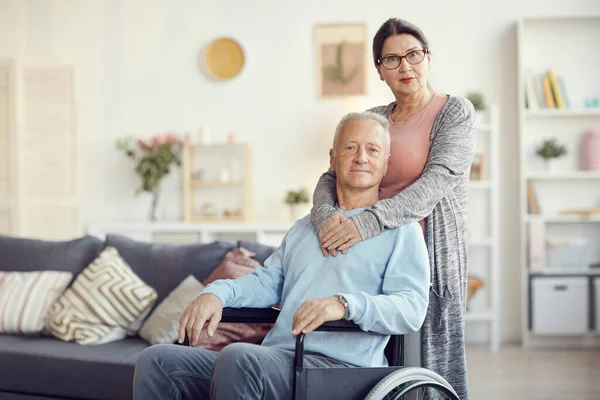 stock image Portrait of content attractive wife in eyeglasses embracing husband in wheelchair around neck while helping him in recovery