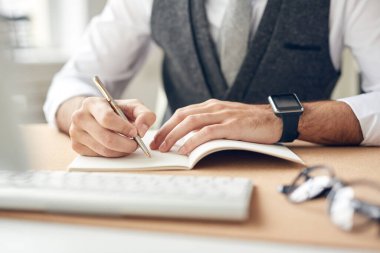 Tanımlanamayan iş adamının resmi. Akıllı adam masada oturuyor ve iş planları yaparken çizim defterine notlar alıyor.